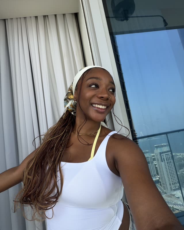 Steph smiling in a white top and headscarf by a high-rise window in Dubai