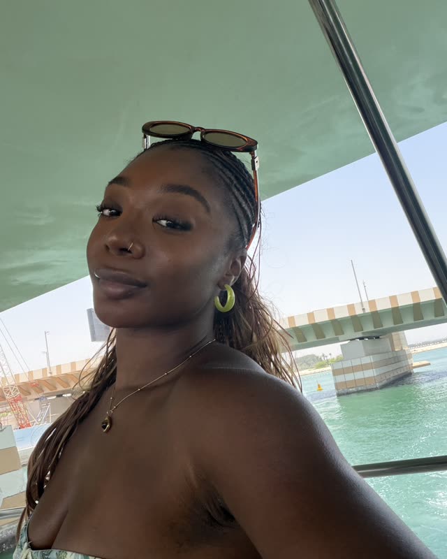 Steph taking a selfie on a boat on the water in Dubai, sunglasses on her head