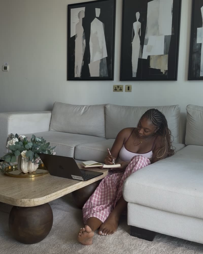Steph sitting on the floor by her sofa, writing in a notebook next to her laptop