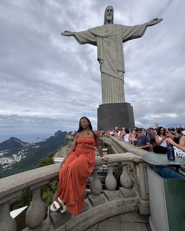 Steph in an orange dress sitting on the balustrade beneath Christ the Redeemer in Rio